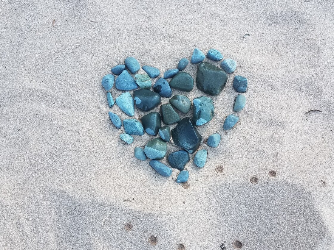 A heart arranged from teal stones on the sand at Lake Superior