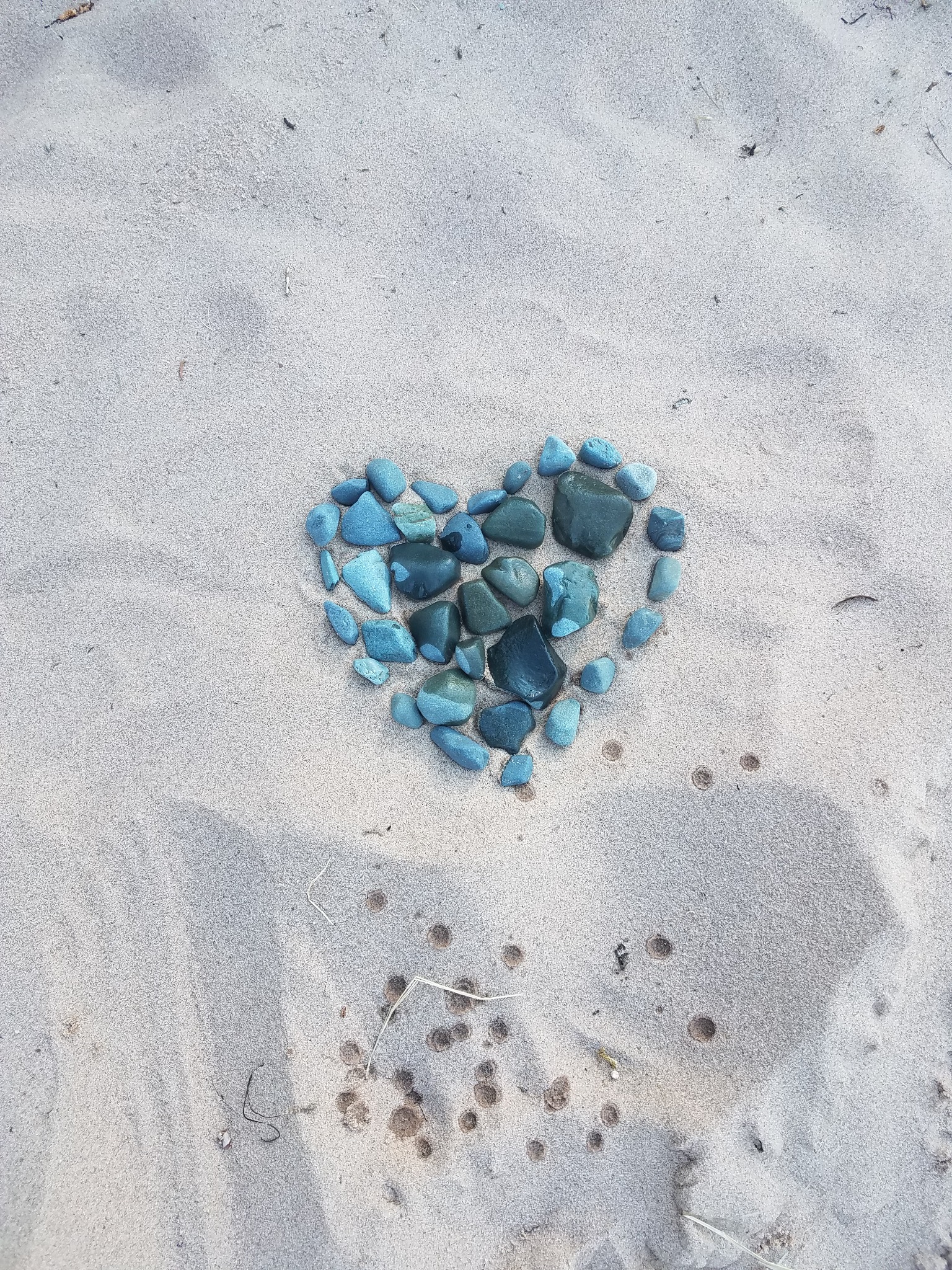 A heart arranged from teal stones on the sand at Lake Superior